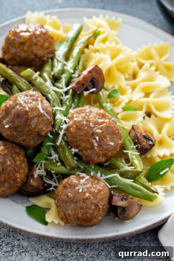 close up picture of cooked ground turkey meatballs with green beans, mushrooms, and pasta on white plate, emphasizing the vibrant colors and appealing texture of the meal