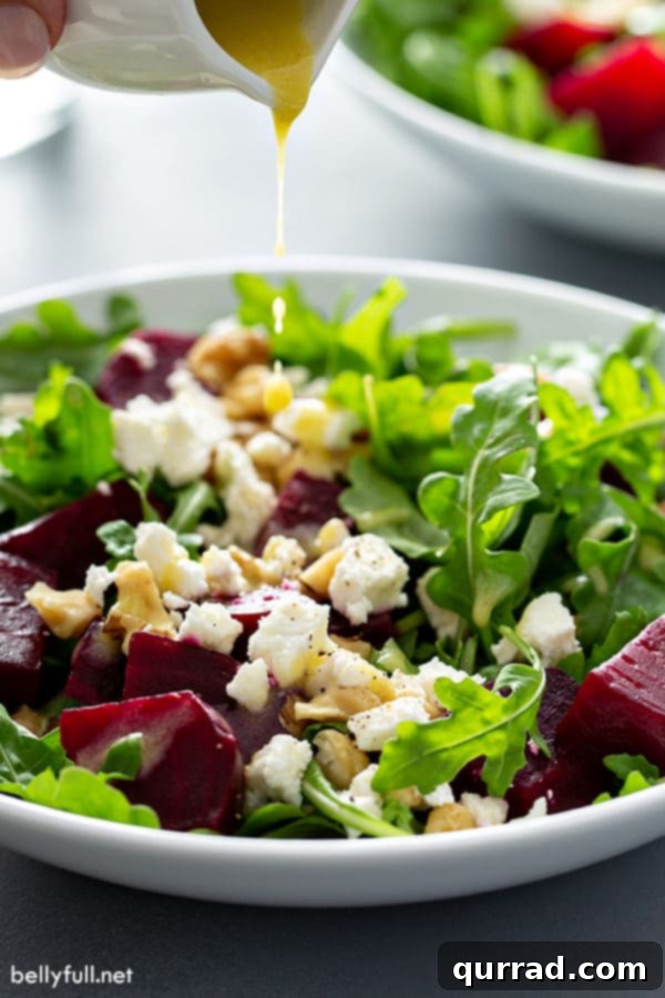 Front angle view of Arugula Beet Salad with a light citrus vinaigrette dressing being poured over the top, highlighting the fresh ingredients