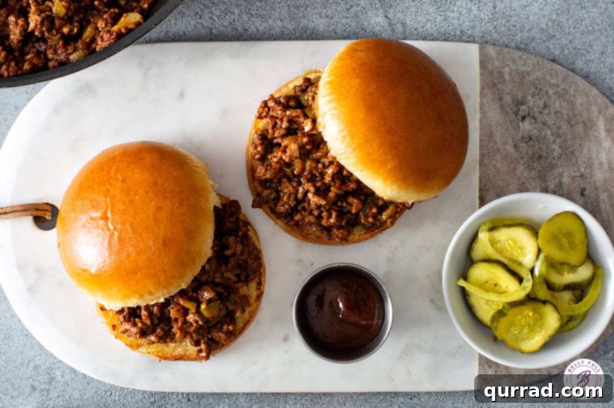 Quick and Craveable Sloppy Joes 4 Overhead shot of two sloppy joes on buns, accompanied by dill pickle spears, on a wooden board.