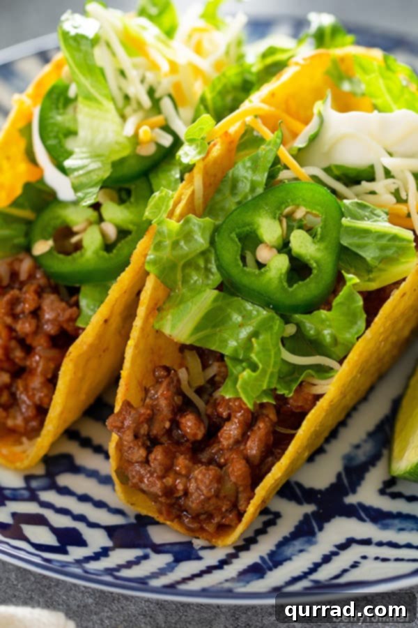 close up of crispy beef taco topped with lettuce and slice jalapenos on blue and white plate