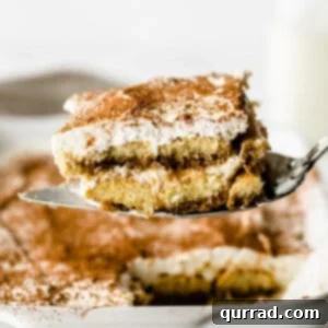 Piece of Tiramisu dessert on metal serving spoon over white casserole dish