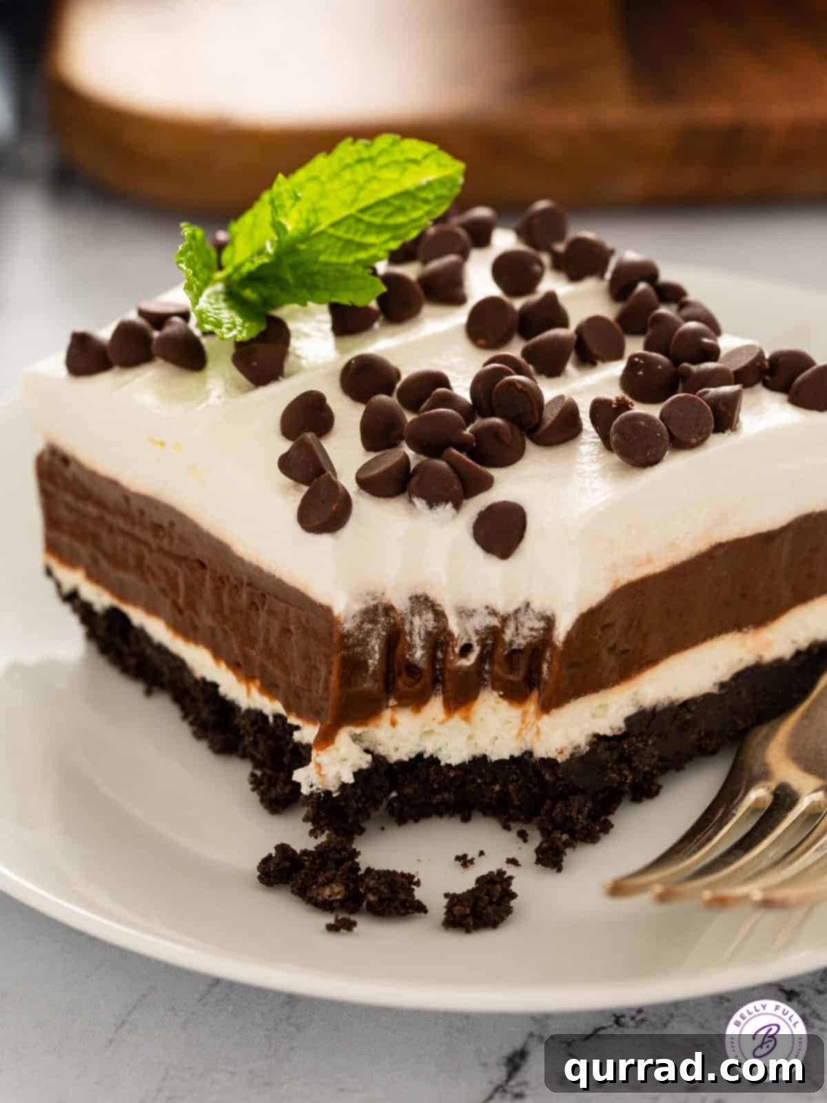 A close-up shot of a square piece of Chocolate Lasagna, or Oreo Lush, with a bite taken out, revealing the distinct delicious layers.