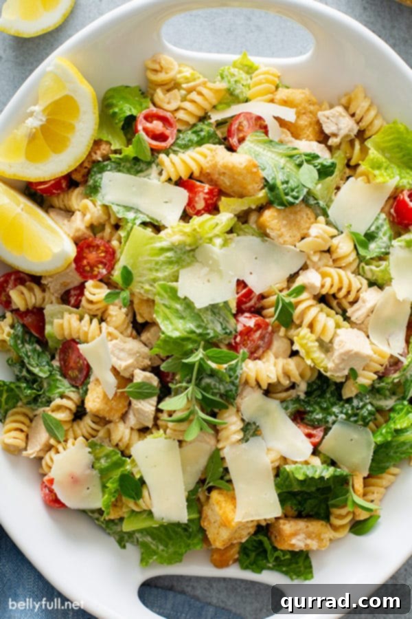 Overhead photo of a serving dish filled with Chicken Caesar Pasta Salad, garnished with fresh Parmesan shavings and lemon wedges, showcasing the colorful ingredients.