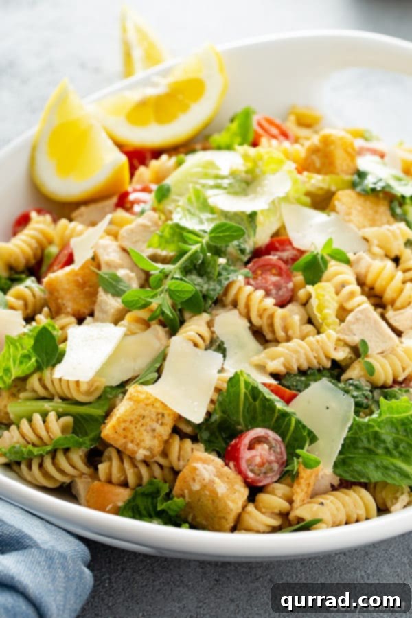 Chicken Caesar Pasta Salad in a white serving dish, garnished with shaved Parmesan, fresh parsley, and a lemon wedge, ready to be served.