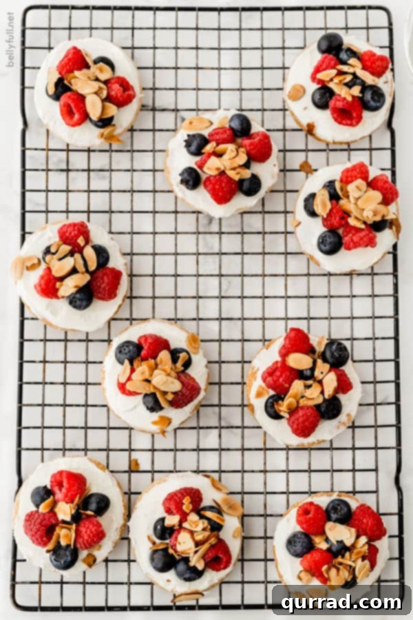 Overhead shot of mini fruit tarts with raspberries and blueberries cooling on a rack, showcasing their perfect round shape and colorful toppings.