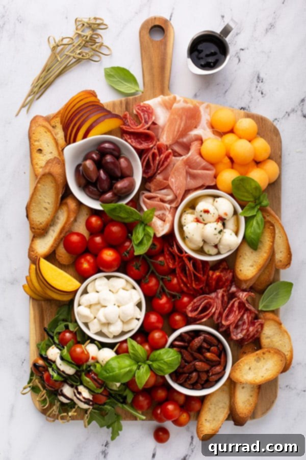 A beautifully arranged rectangular Italian antipasto charcuterie board featuring Galbani mozzarella balls, a variety of cured meats like prosciutto and salami, vibrant fresh peaches, juicy cherry tomatoes, toasted baguette slices, Kalamata olives, and a drizzle of balsamic glaze.