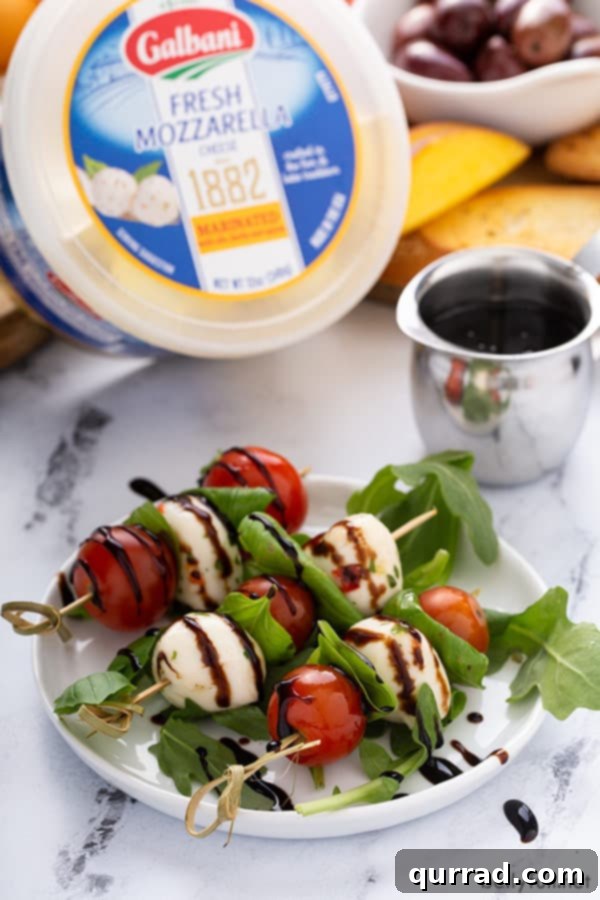 Close-up of individual caprese appetizer skewers, featuring fresh Galbani mozzarella pearls, vibrant cherry tomatoes, and basil leaves, expertly drizzled with a rich balsamic glaze on a pristine white plate.