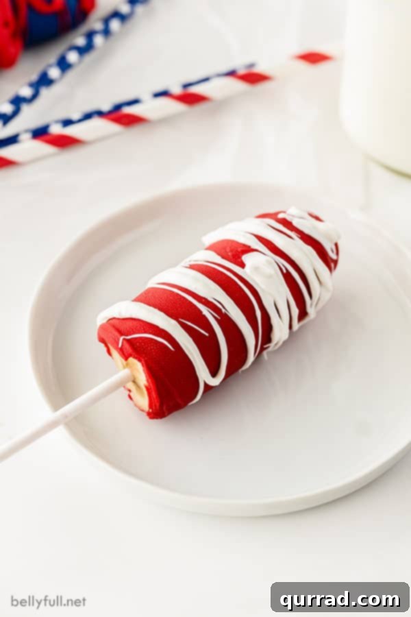 half a frozen banana coated in red chocolate drizzled with white chocolate on a white plate