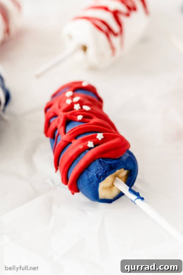 half a frozen banana with lollipop stick, coated in blue chocolate drizzled with red chocolate on a white plate