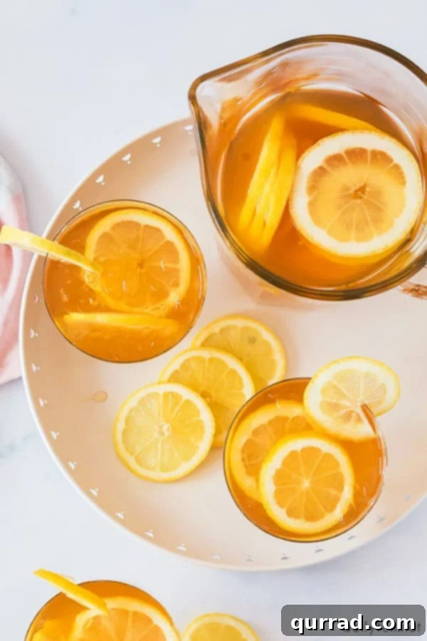 Southern Sweet Tea Classic 5 Overhead view of two glasses and a large pitcher filled with sweet tea and sliced lemons, indicating a generous serving size.