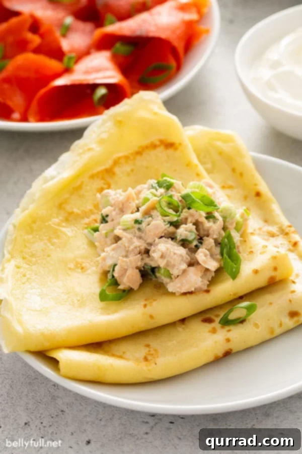 Authentic Russian Blini Recipe 5 folded crepes on white plate with tuna and scallions