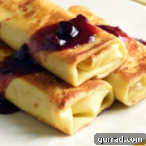 Close-up of three golden-brown blintzes on a white plate, garnished with a dollop of jam and powdered sugar.