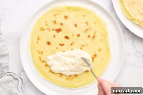 Blintz Bliss 6 Cheese filling being carefully spooned onto the lower third of a thin crepe.