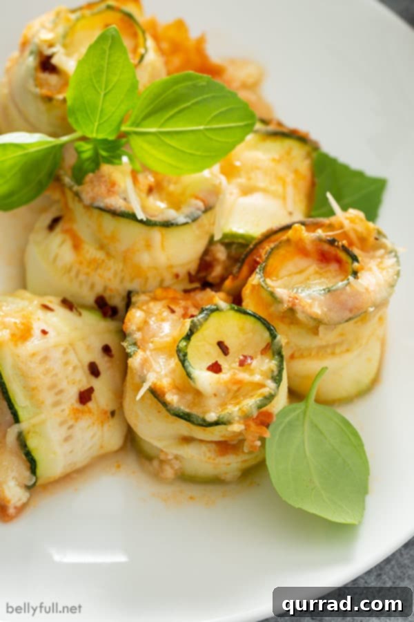 Close-up photograph of perfectly baked zucchini lasagna rolls, arranged upright on a pristine white plate and garnished with vibrant green basil leaves, highlighting their beautiful spiral shape.