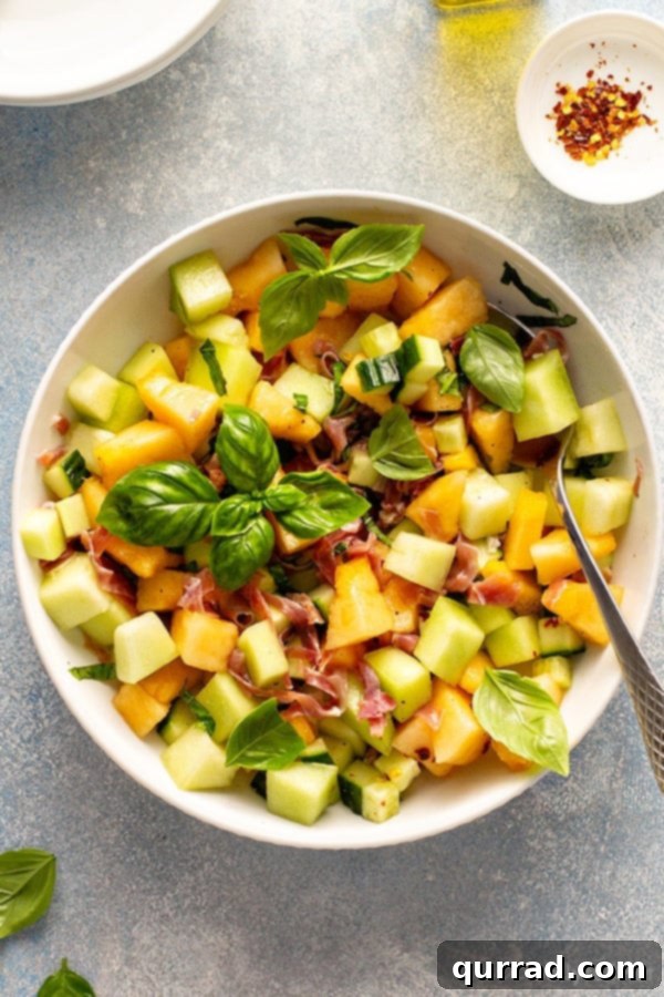 Overhead view of a vibrant Melon Cucumber Salad in a white serving bowl, garnished with fresh basil leaves, evoking summer freshness.