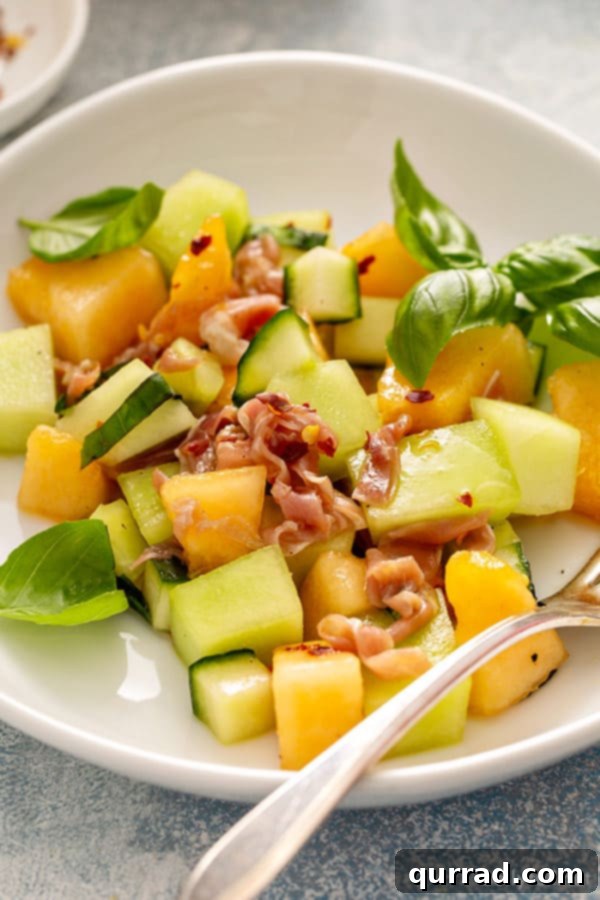 Close-up detailed shot of Melon Cucumber Salad on a white plate, ready to be enjoyed with a fork.