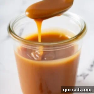 Homemade caramel sauce dripping from a spoon, illustrating its rich, smooth texture and golden color.