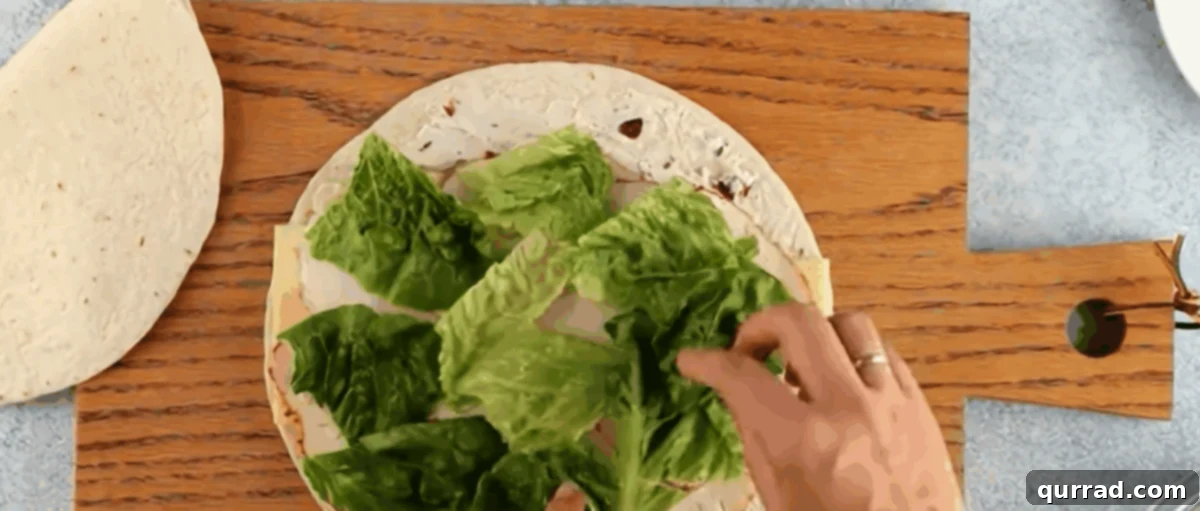 Spiral Chicken Salad Bites 9 Adding romaine lettuce over the chicken and cheese layers on the tortilla.