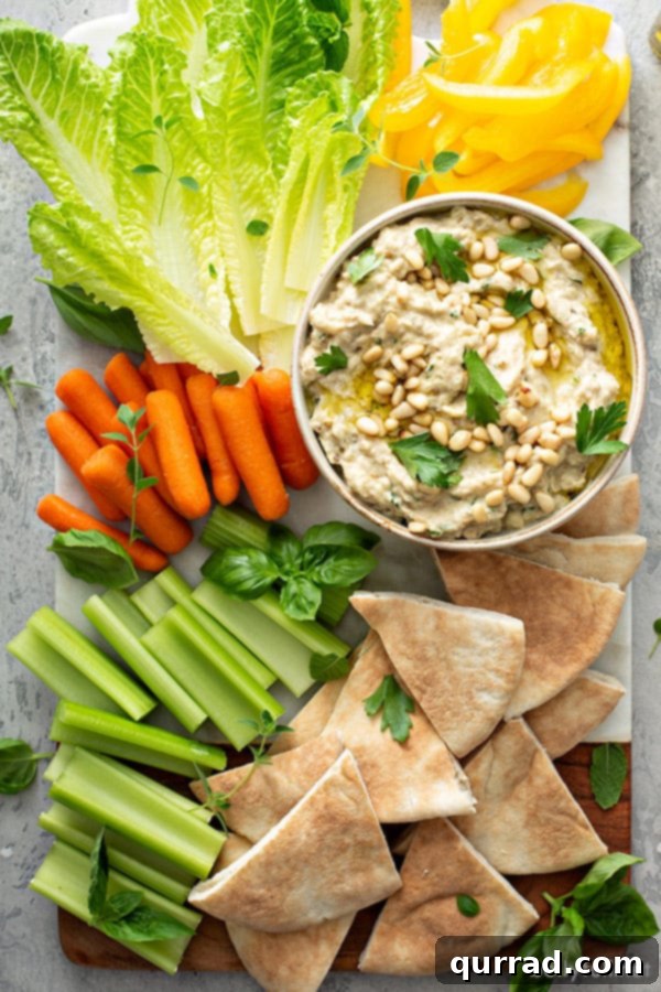 overhead of baba ganoush in white serving dish surrounded by carrots, celery, bell pepper, and pita wedges