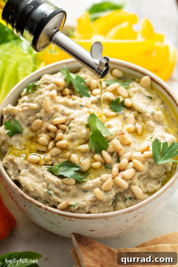 baba ganoush in serving bowl garnish with pine nuts and fresh chopped parsley with olive oil drizzle