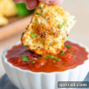 One toasted ravioli being dipped in marinara sauce, showcasing its perfectly crispy texture.