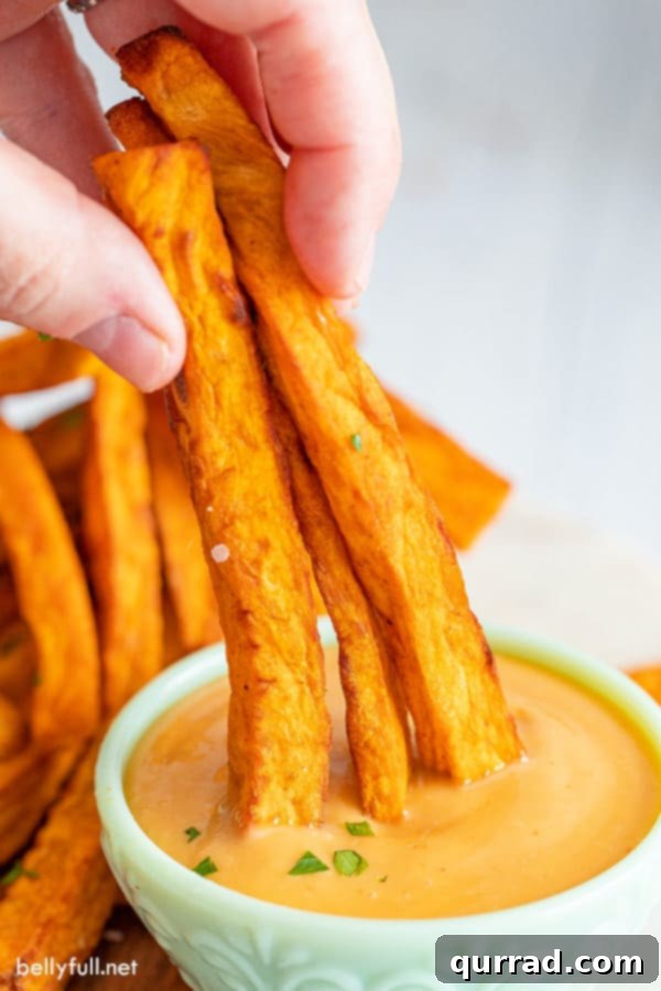 Crispy Sweet Potato Fries Air Fryer or Oven 5 Three perfectly golden sweet potato fries being dipped into a creamy, savory sauce, ready to be enjoyed.