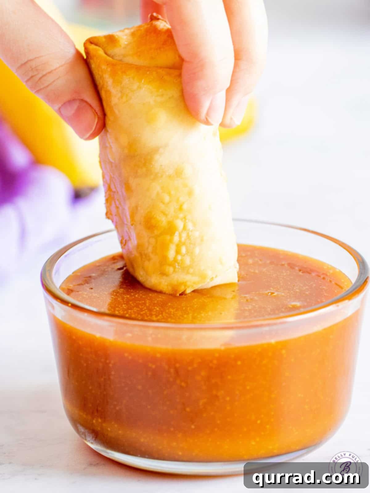 Crispy Air-Fried Banana Rolls 3 A perfectly air-fried banana lumpia being dipped into a bowl of rich, homemade caramel sauce.