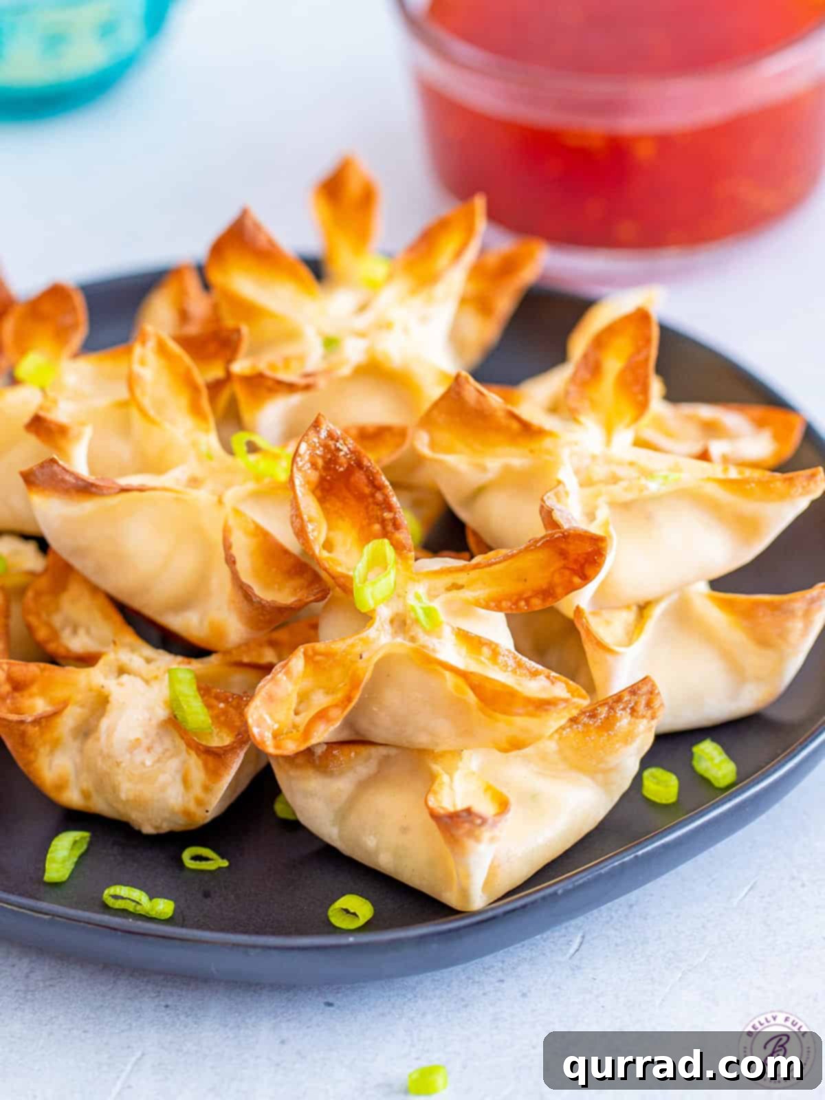 A beautifully arranged plate full of golden, crispy air fryer crab rangoon, garnished and ready for dipping.