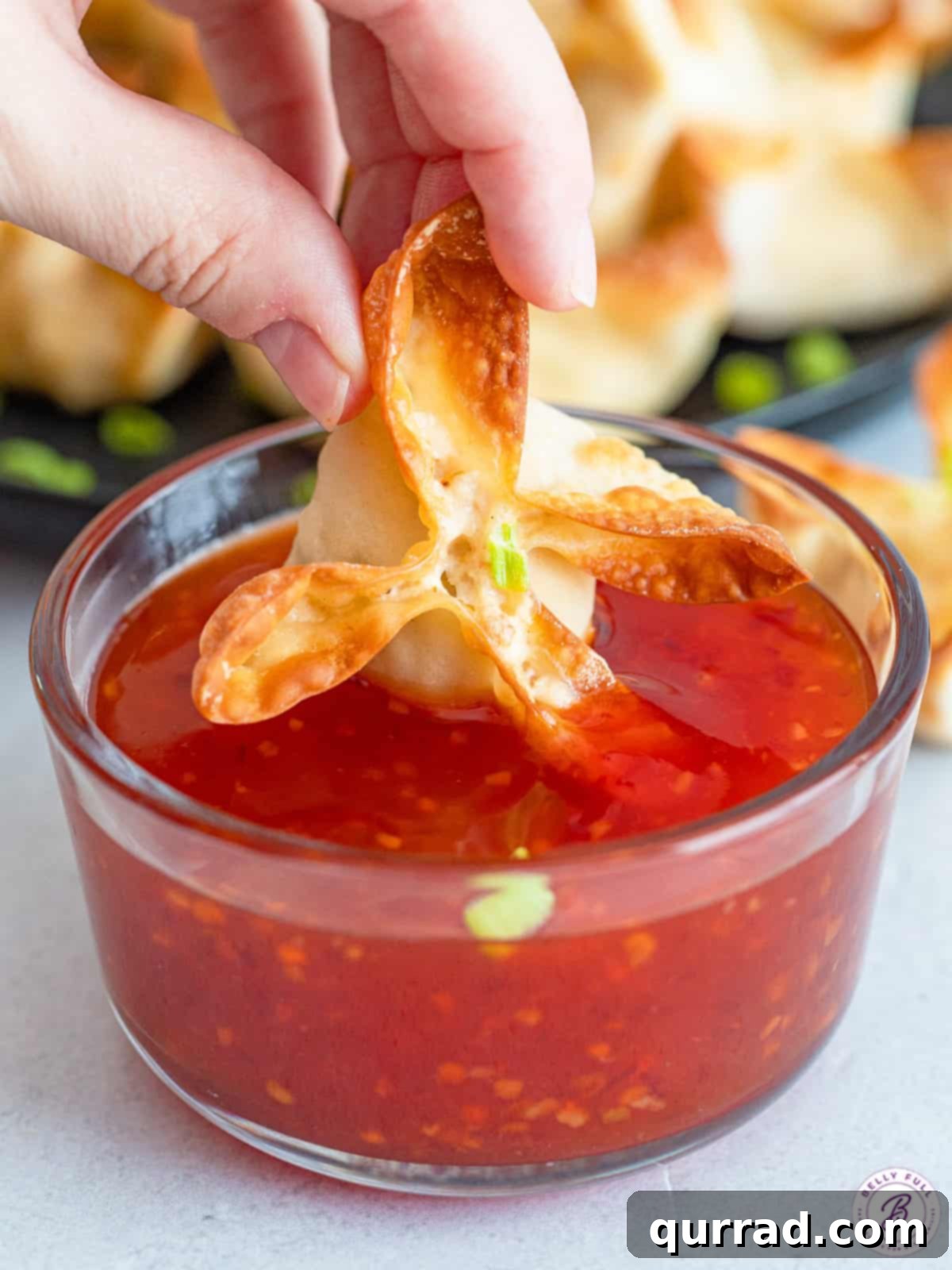 Crispy golden crab rangoon being dipped into a bowl of homemade sweet chili sauce, perfectly highlighting its delectable texture.