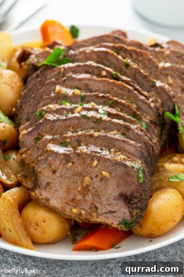 Melt in Your Mouth Slow Cooker Pot Roast 6 Sliced cooked pot roast with gravy over tender vegetables on a white serving platter.