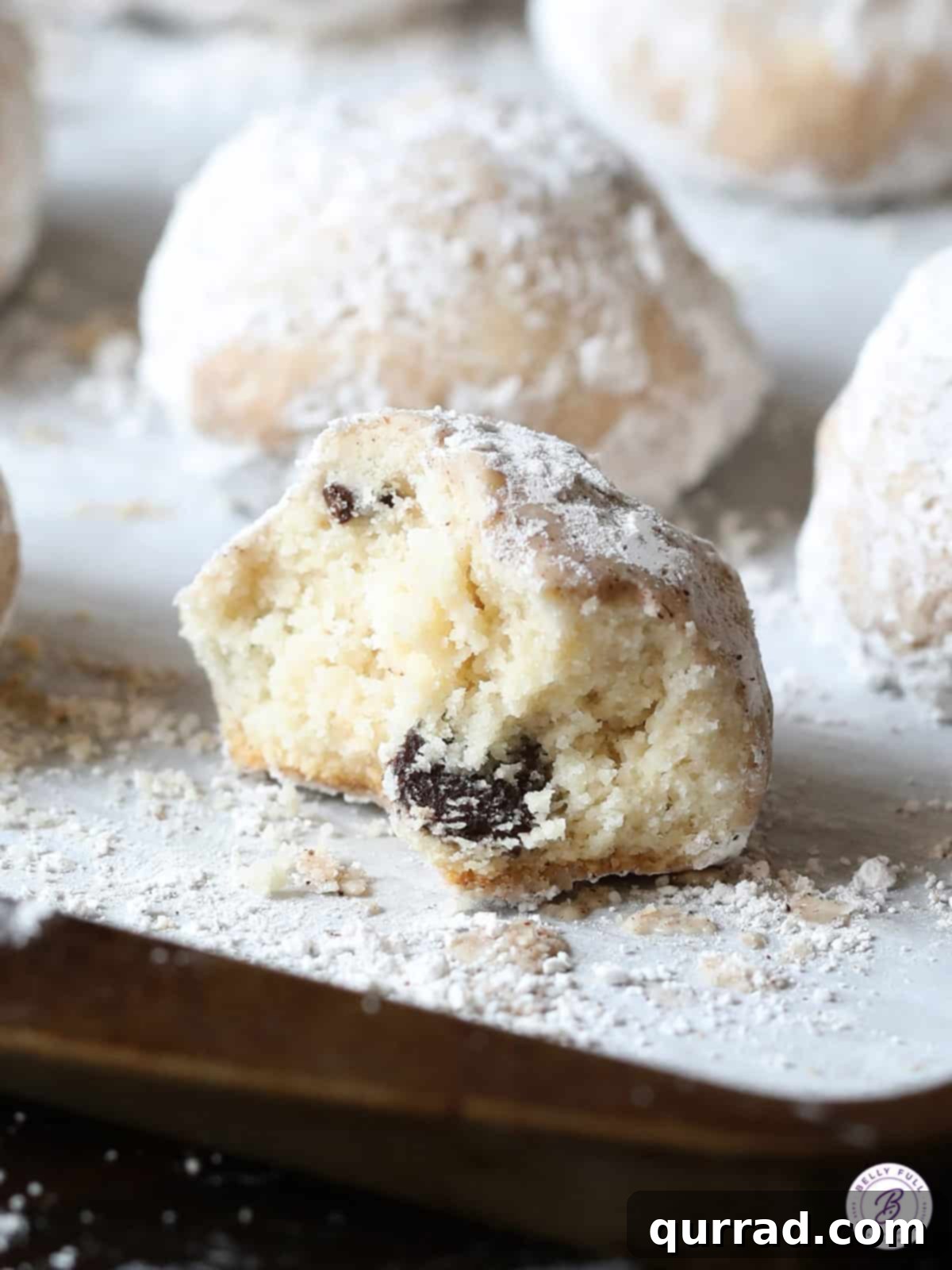 Close-up of a single Snowball Cookie with a bite taken out, revealing the soft interior and chocolate chips, resting on a baking sheet.