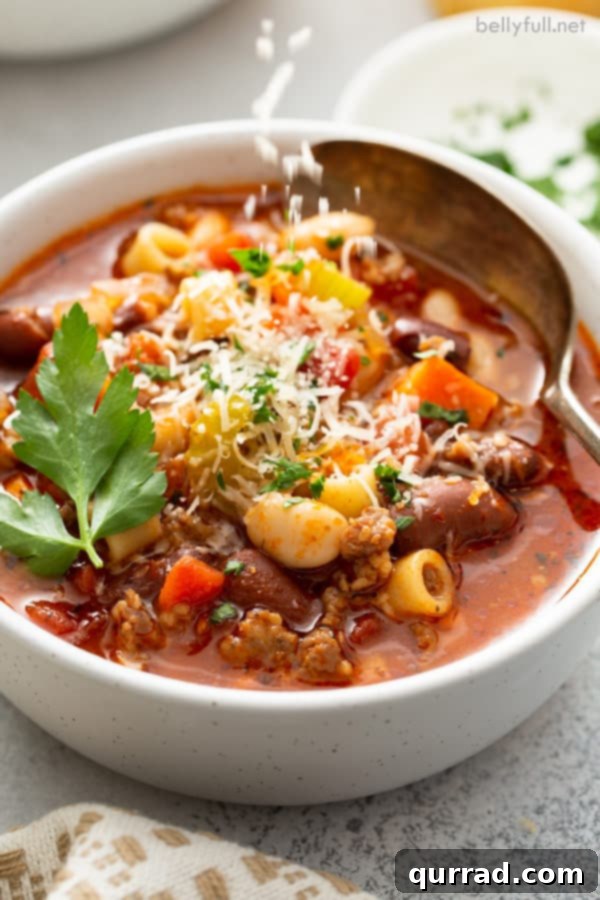 Homemade Olive Garden Pasta Fagioli Soup 5 A white bowl of Pasta Fagioli soup, garnished with a generous sprinkle of Parmesan cheese.