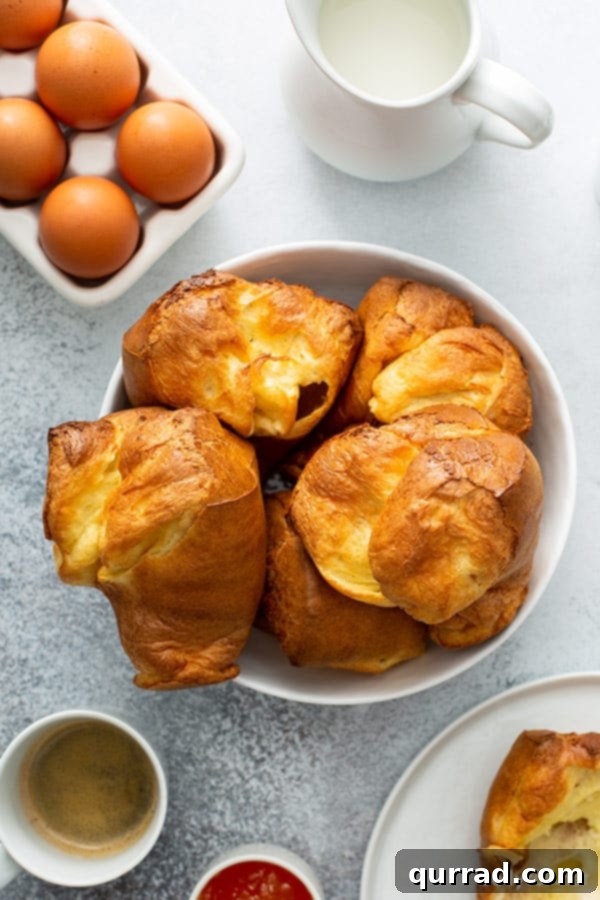Baked golden popovers piled high in a white serving bowl, light and fluffy.