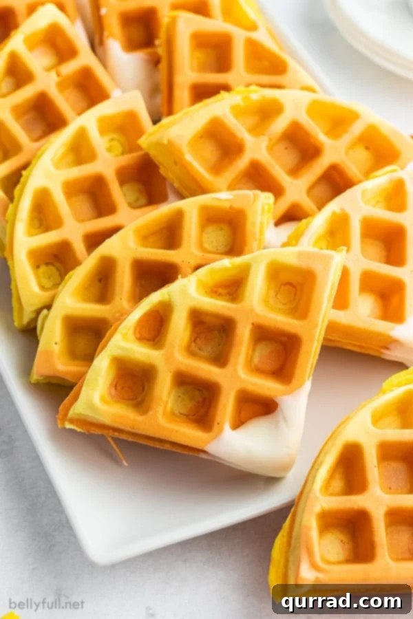 Close-up of freshly made Candy Corn Colored Waffles cut into vibrant yellow and orange triangles with white tips, arranged appealingly on a plate.