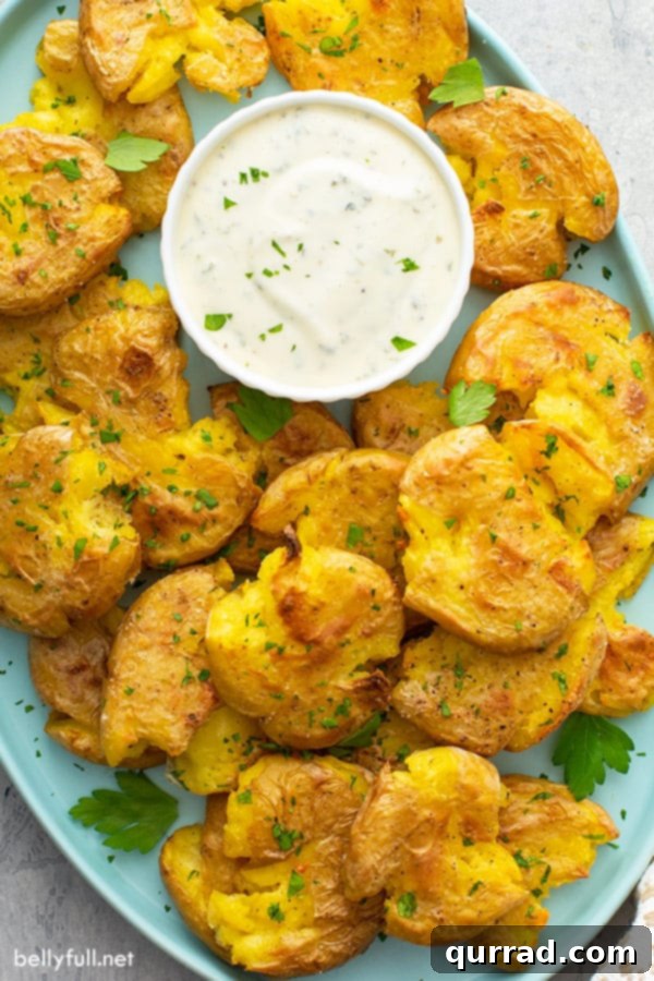 Golden Crispy Smashed Potatoes 6 An overhead shot of a generous pile of roasted smashed potatoes on a serving tray, accompanied by a small bowl of dipping sauce.