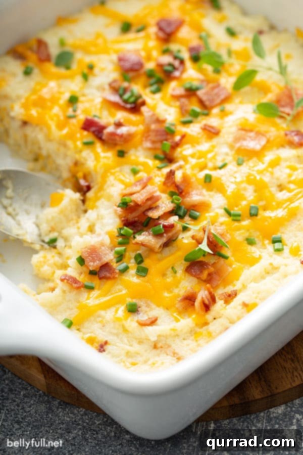 Ultimate Loaded Cauliflower Bake 3 Close-up shot of baked mashed cauliflower casserole in a white dish, beautifully garnished with crumbled cooked bacon and a hint of green herbs.