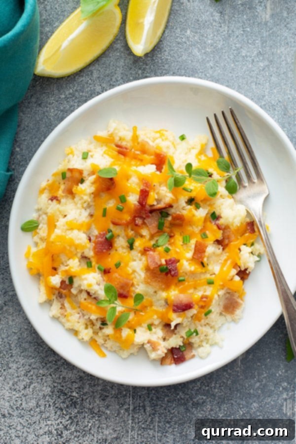 Ultimate Loaded Cauliflower Bake 4 Overhead shot of a serving of cauliflower mash on a white plate with a fork, showing its creamy texture.