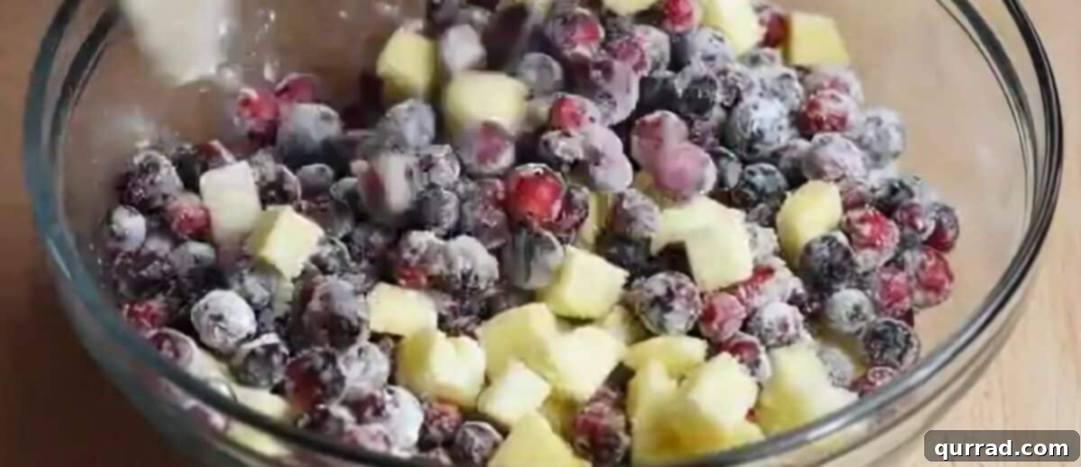 A glass bowl filled with diced apples and cranberries, tossed with sugar, flour, vanilla, and orange juice, ready for baking.