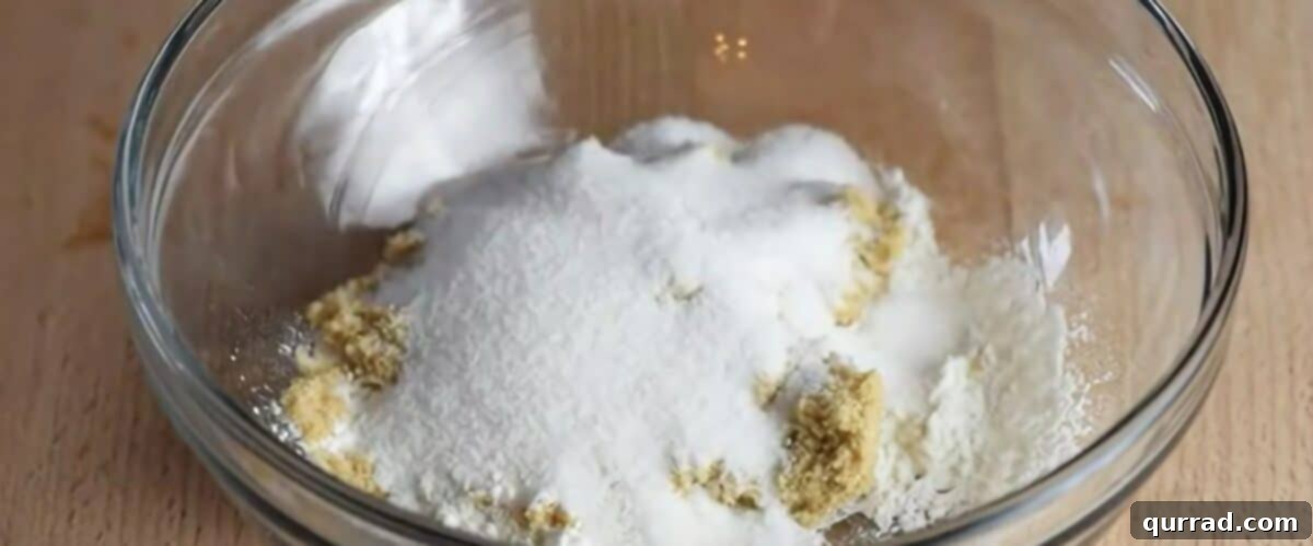 Hands combining flour, sugars, pecans, cinnamon, and cubed cold butter in a glass bowl to create a crumbly topping for the crisp.