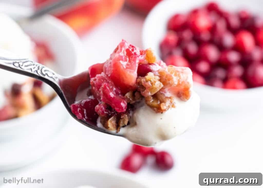 A close-up shot of a spoon scooping a portion of baked apple cranberry crisp, revealing the tender fruit and crunchy topping.