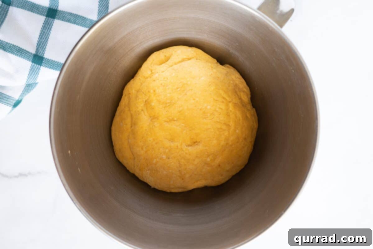 Autumn Spice Pumpkin Rolls 6 A bowl of pumpkin cinnamon roll dough, visibly proofed and expanded after its first rise.
