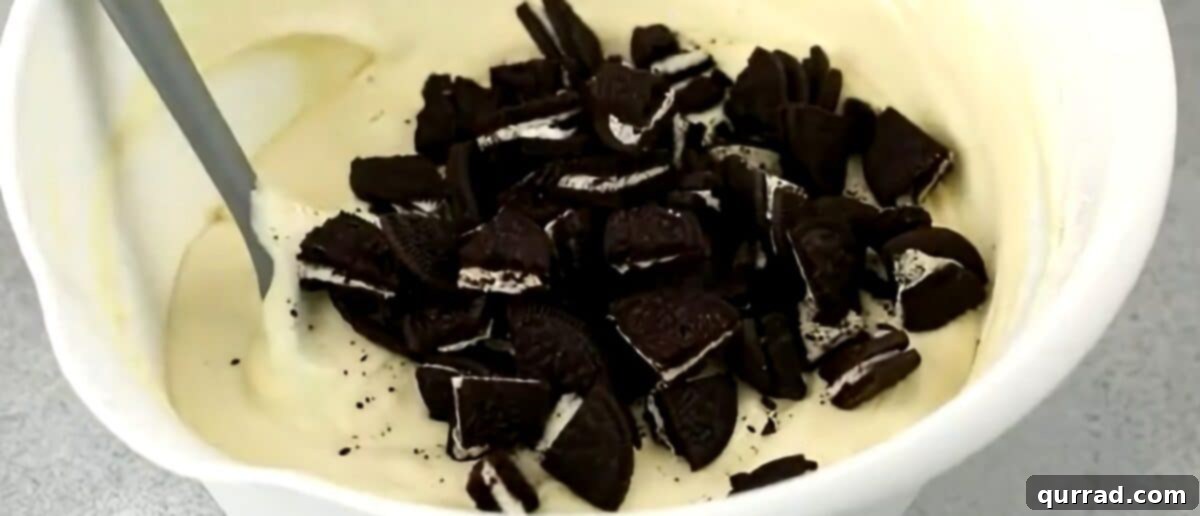Decadent Oreo Cheesecake 7 Folding quartered Oreo cookies into the cheesecake filling with a rubber spatula.