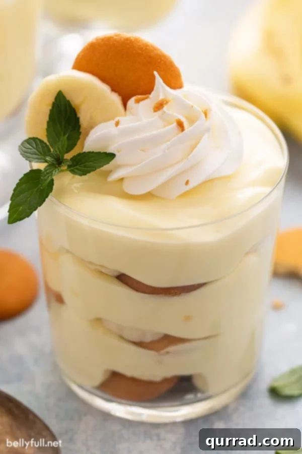 close up of banana pudding in a glass, garnished with whipped cream and a mint leaf