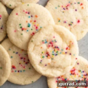 Overhead shot of a pile of golden-brown sugar cookies with colorful sprinkles, indicating a recipe.