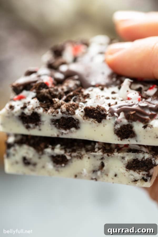 Arctic Mint Oreo Brittle 5 A close-up image of a thick piece of Peppermint Oreo Bark, cleanly cut in half to reveal the distinct layers of white and dark chocolate, crushed Oreos, and embedded peppermint pieces, emphasizing its delightful texture.