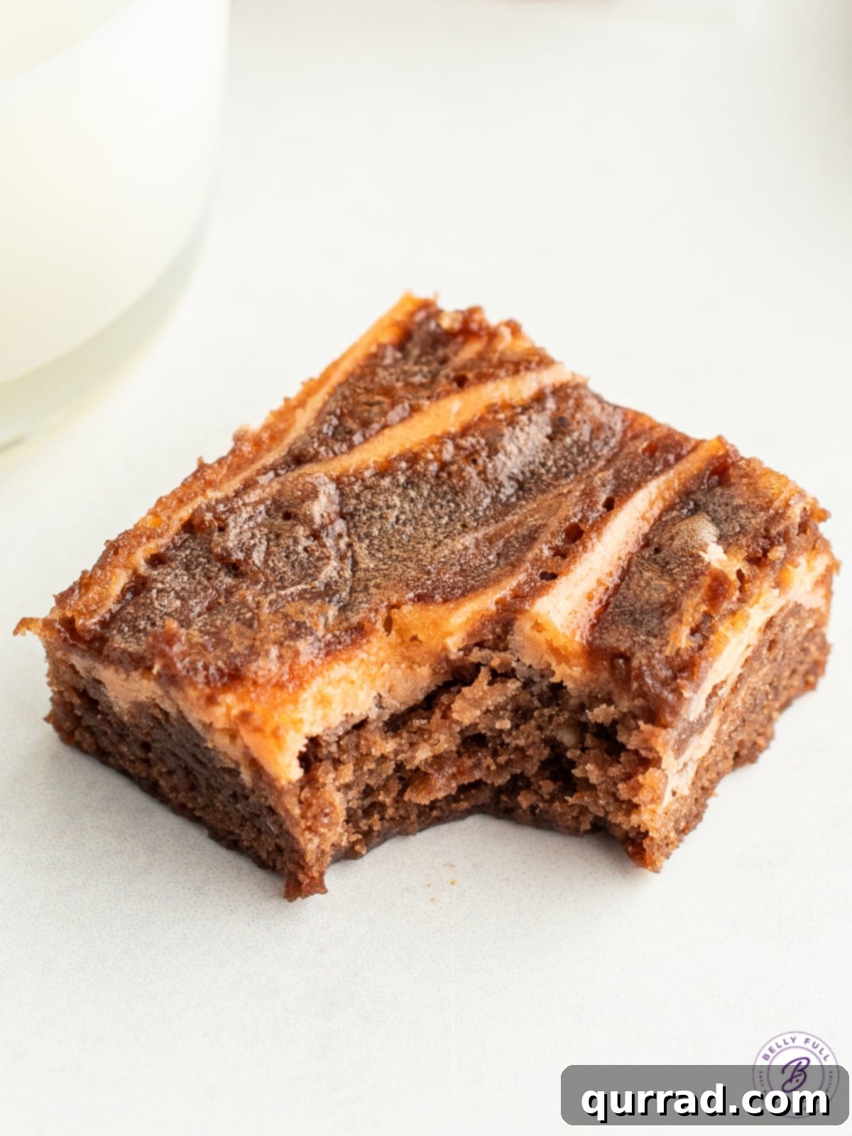 A Halloween brownie with a bite taken out, revealing its fudgy interior and vibrant orange cream cheese swirl.