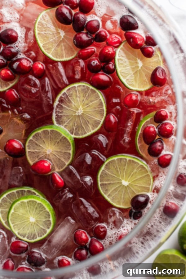 Effortless Festive Drink 2 Overhead close-up of a vibrant holiday punch, garnished with glistening cranberries and fresh lime slices, invitingly arranged for a festive gathering.