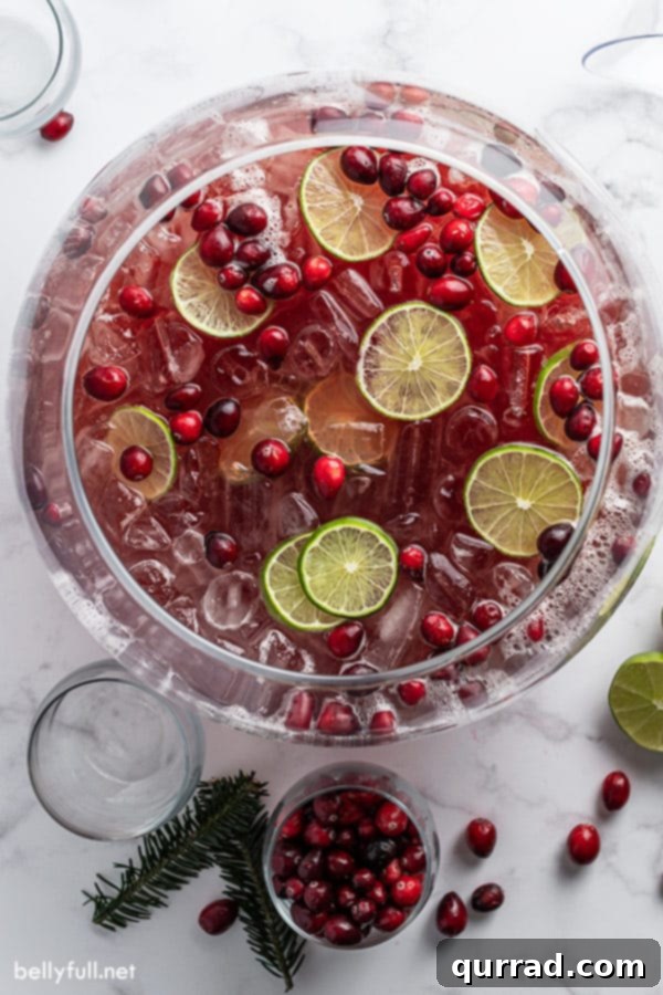 Effortless Festive Drink 3 An inviting overhead shot of a large glass punch bowl filled with holiday punch, beautifully adorned with floating cranberries and bright lime slices, ready for serving.