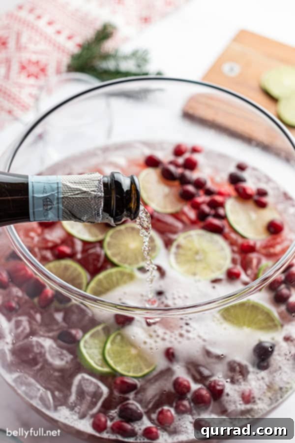 Effortless Festive Drink 4 Sparkling Prosecco wine being elegantly poured into a large, crystal punch bowl filled with the holiday punch mixture.