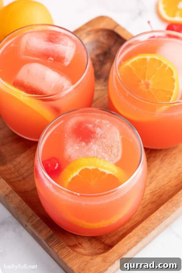 Overhead view of a glass filled with Shirley Temple Party Punch, featuring a colorful array of ice cubes with cherries, orange slices, and a vibrant red liquid.
